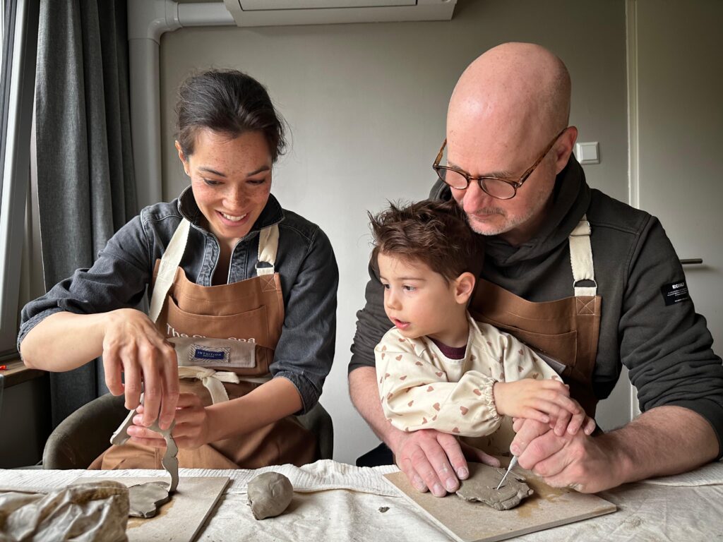 A family participating in the Family Ceramic Experience at The Clay Spa, gathered closely as a son sits on his father's lap and everyone looks at the ceramic creation in the mother's hands