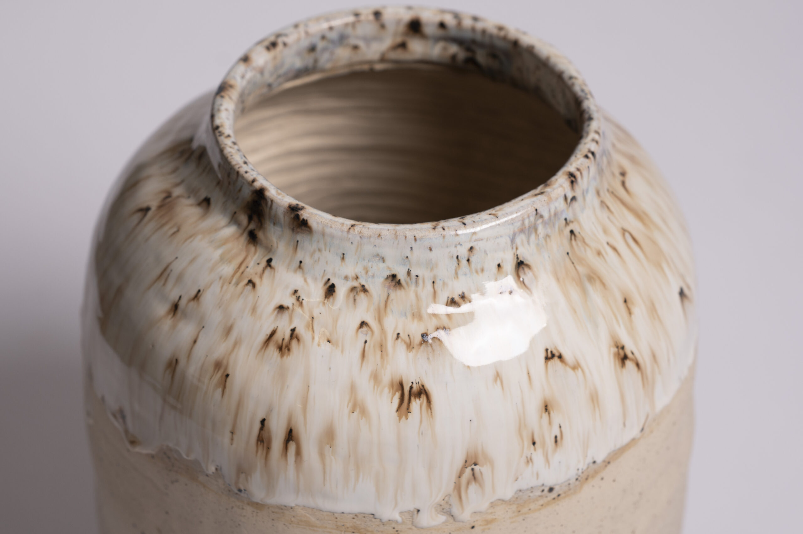 A large archival ceramic vase, showcasing a beautiful glossy white glaze with rustic brown speckles on its surface 1